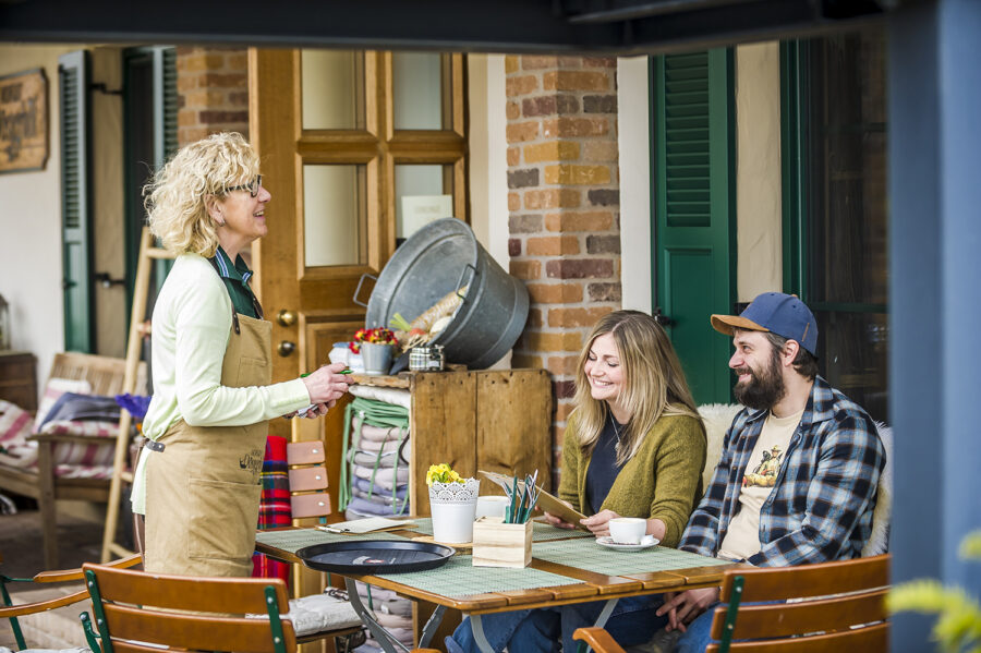 Spaß an der Arbeit - Servicemitarbeiterin mit Paar auf der Terrasse vor dem Hofcafé