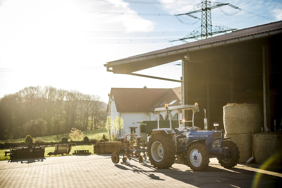 Ford Traktor am Kuhstall mit Heuballen im Sonnenlicht