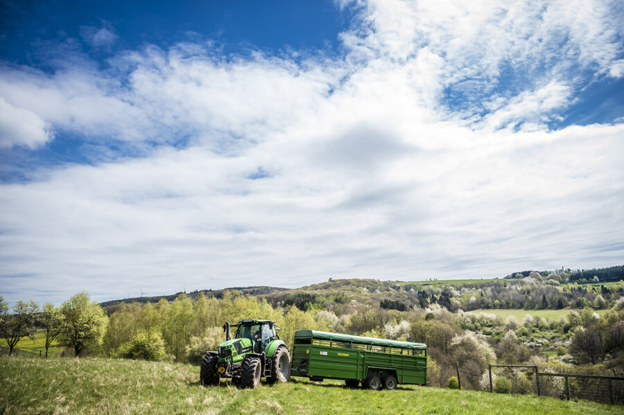 Traktor Deutz-Fahr mit Viehanhänger auf den Weiden vor den blühenden Strohobstwiesen