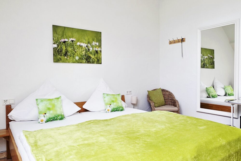Blick von der Badezimmertür aus auf das Bett und den Ganzkörperspiegel im Hotelzimmer Gänseblümchen