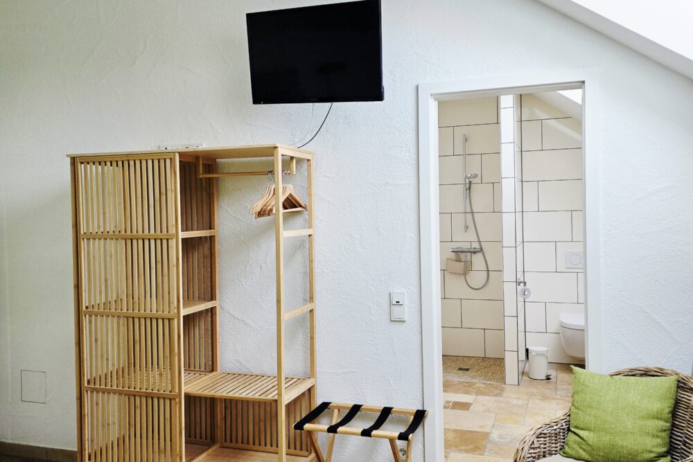 Blick vom Bett aus auf offenen Schrank, Tür ins Bad, Sessel im Hotelzimmer Gänseblümchen