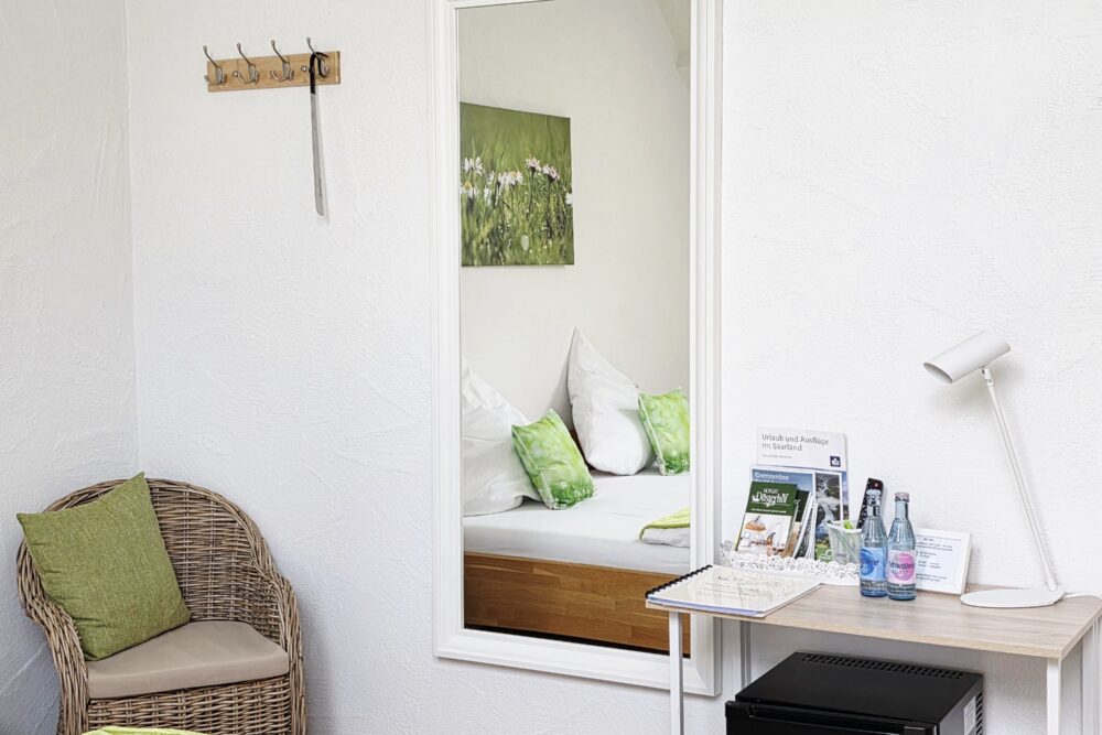 Schreibtisch mit Tischlampe, Informationen sowie Getränken, Kühlschrank und Ganzkörperspiegel im Hotelzimmer Gänseblümchen