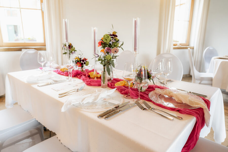 Tischdekoration mit Kerzen, pinkem Tischläufer, Zitrusfrüchten und bunten Blumen